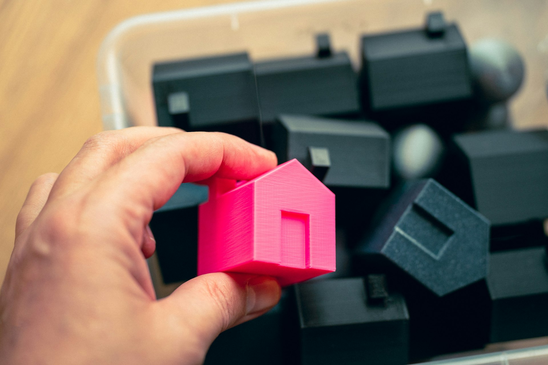 A person holding a pink house in front of a pile of black cubes